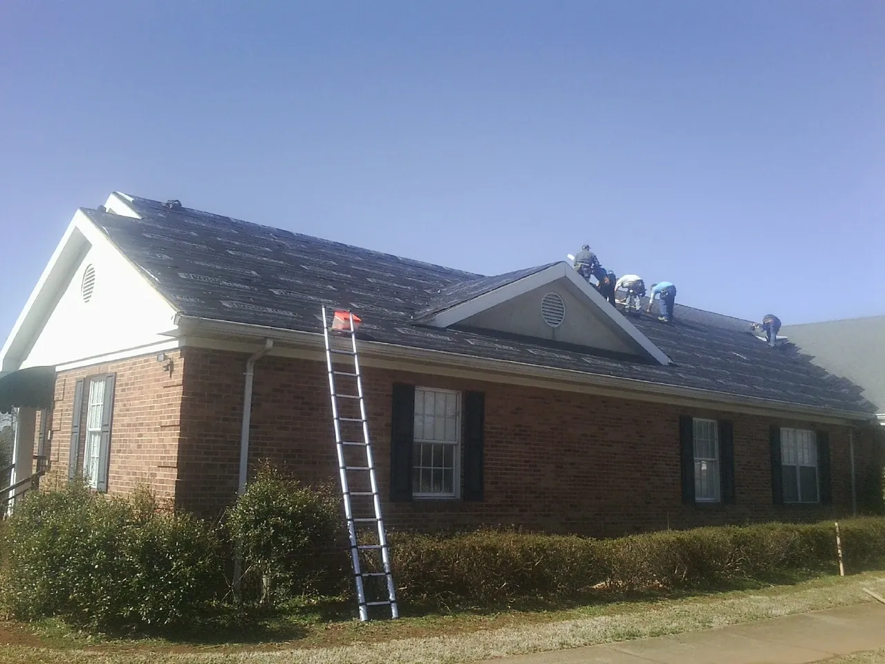 Crew tearing shingles off a brick ranch roof with a ladder set — Emergency Roof Repair work by our crew in Laguna