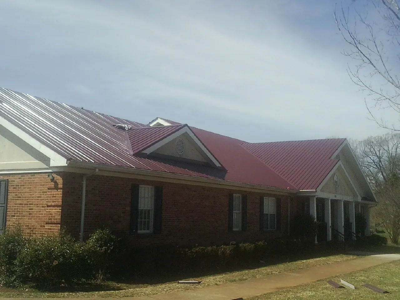 Red metal roof with gabled entries on a long brick building, from a Hail Damage Roof Repair job in Laguna