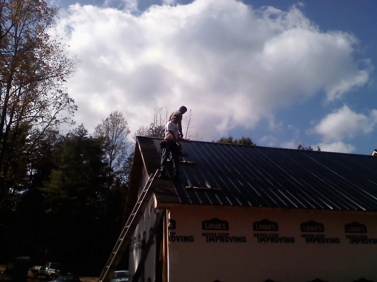 Roofer fastening dark metal panels high against a cloudy sky, from a Roof Inspection job in Laguna