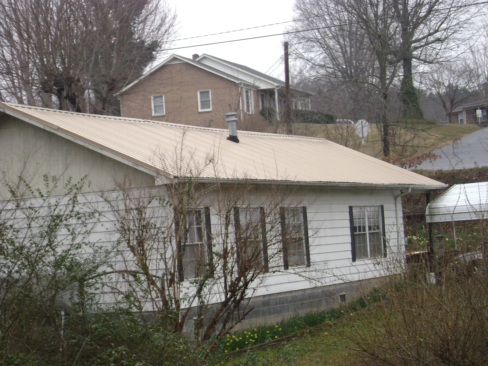 Tan metal roof on a white sided house set into a hillside — Commercial Roofing by Roofing Brothers in Laguna
