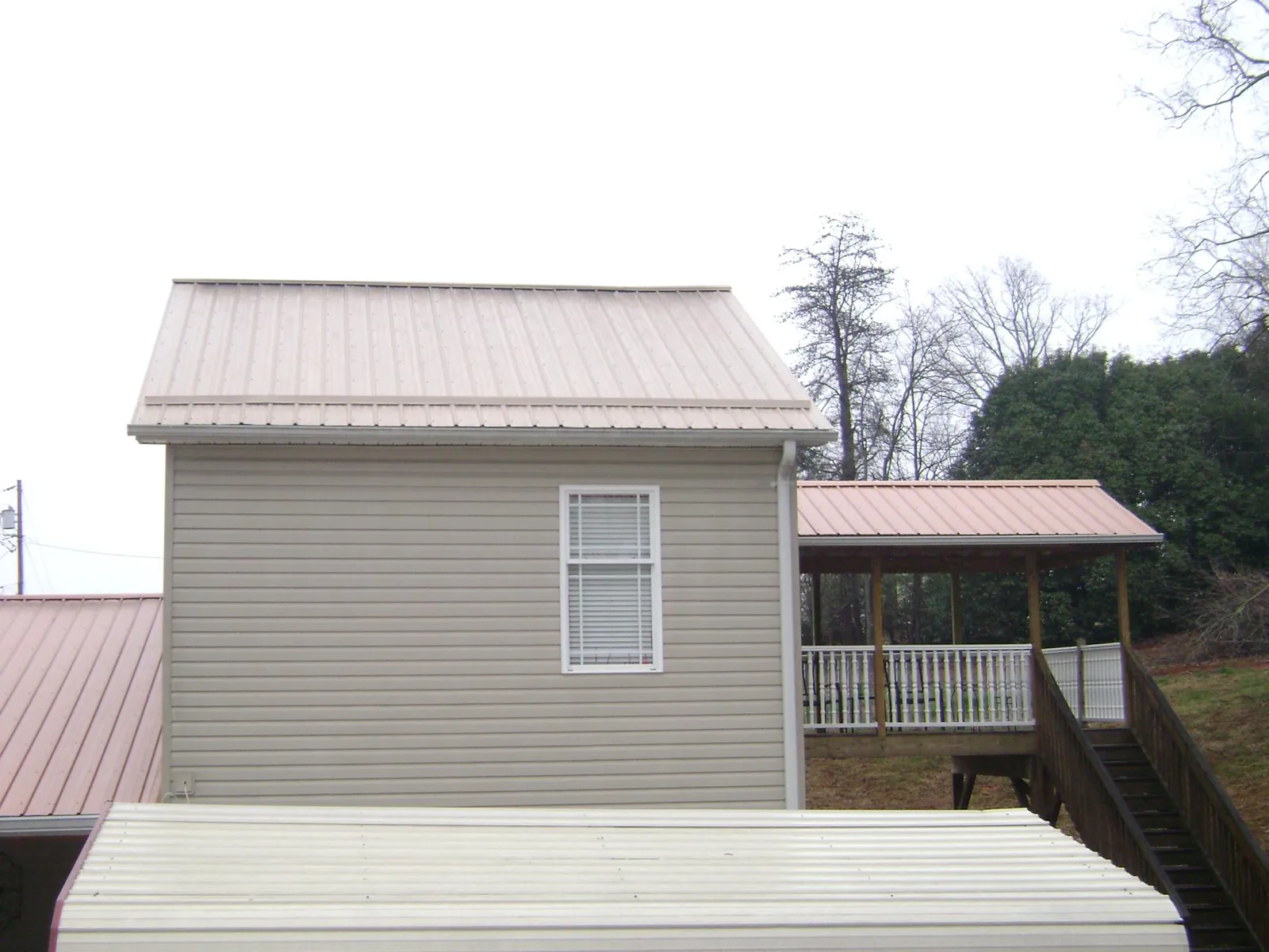 Tan metal roofs on a two story addition and attached porch, from a Roof Replacement job in Laguna
